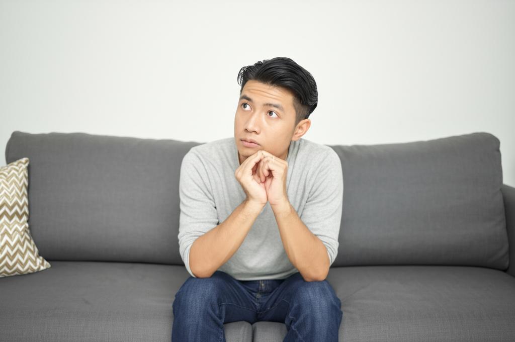 AI prompt: A man sitting on a sofa looking thoughtful and slightly stressed, contemplating his energy levels and relationship.