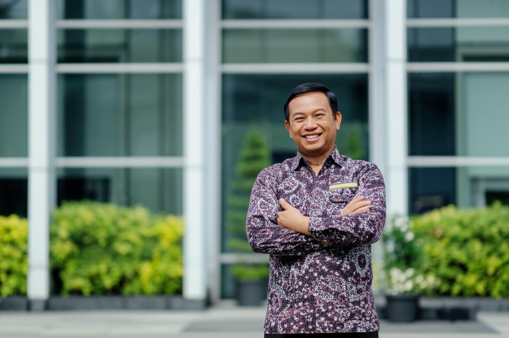 Pak Budi, a smiling middle-aged man, standing confidently in front of his office building, looking energetic and healthy.