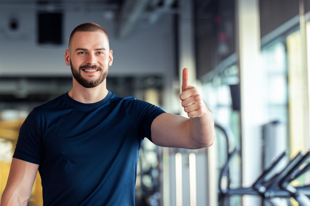 AI prompt: A man looking energetic and happy, giving a thumbs up after a successful workout, feeling refreshed and powerful, bright gym background, realistic photo