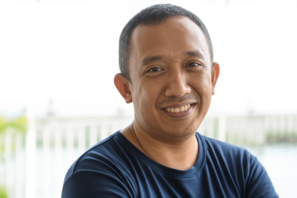 AI prompt: A middle-aged Indonesian man smiling, looking energetic and confident, perhaps enjoying a morning activity or a relaxed moment.